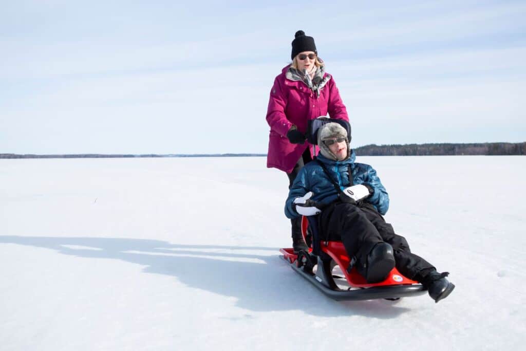 On talvi ja aurinko paistaa. Mies istuu punaisessa kelkassa järven jäällä kasvot kohti kameraa. Hänen takanaan, kelkan jalkalaudalla, seisoo nainen.